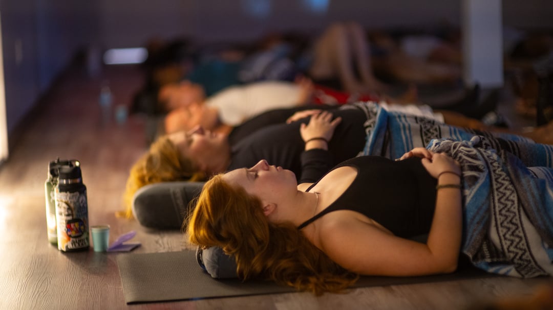 Yoga students resting in savasana on mats with bolsters and blankets in warm, low light during a sound bath at Flow Yoga North Loop.